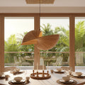 A modern dining room with a round wooden table set with white dishes, surrounded by beige chairs. A large, sculptural wooden pendant light hangs over the table.
