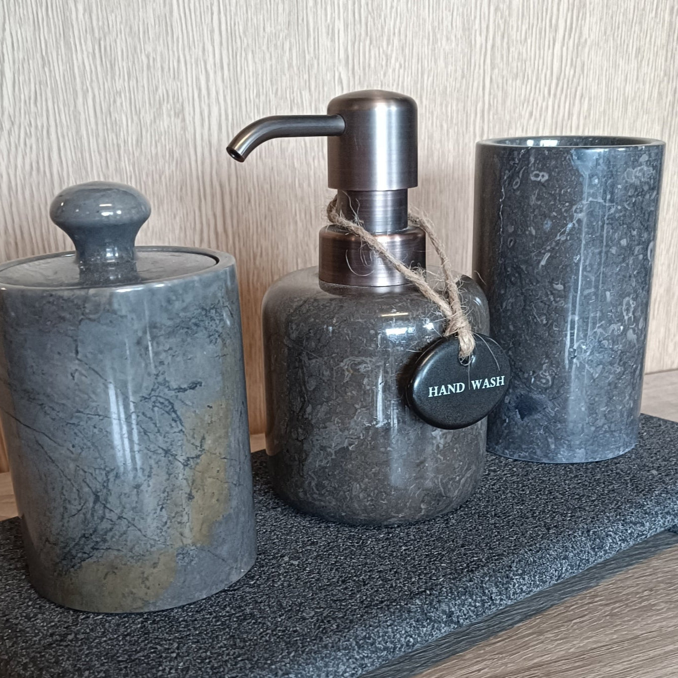 Bathroom accessory set with soap dispenser, jar, and cup on a tray against a wooden background