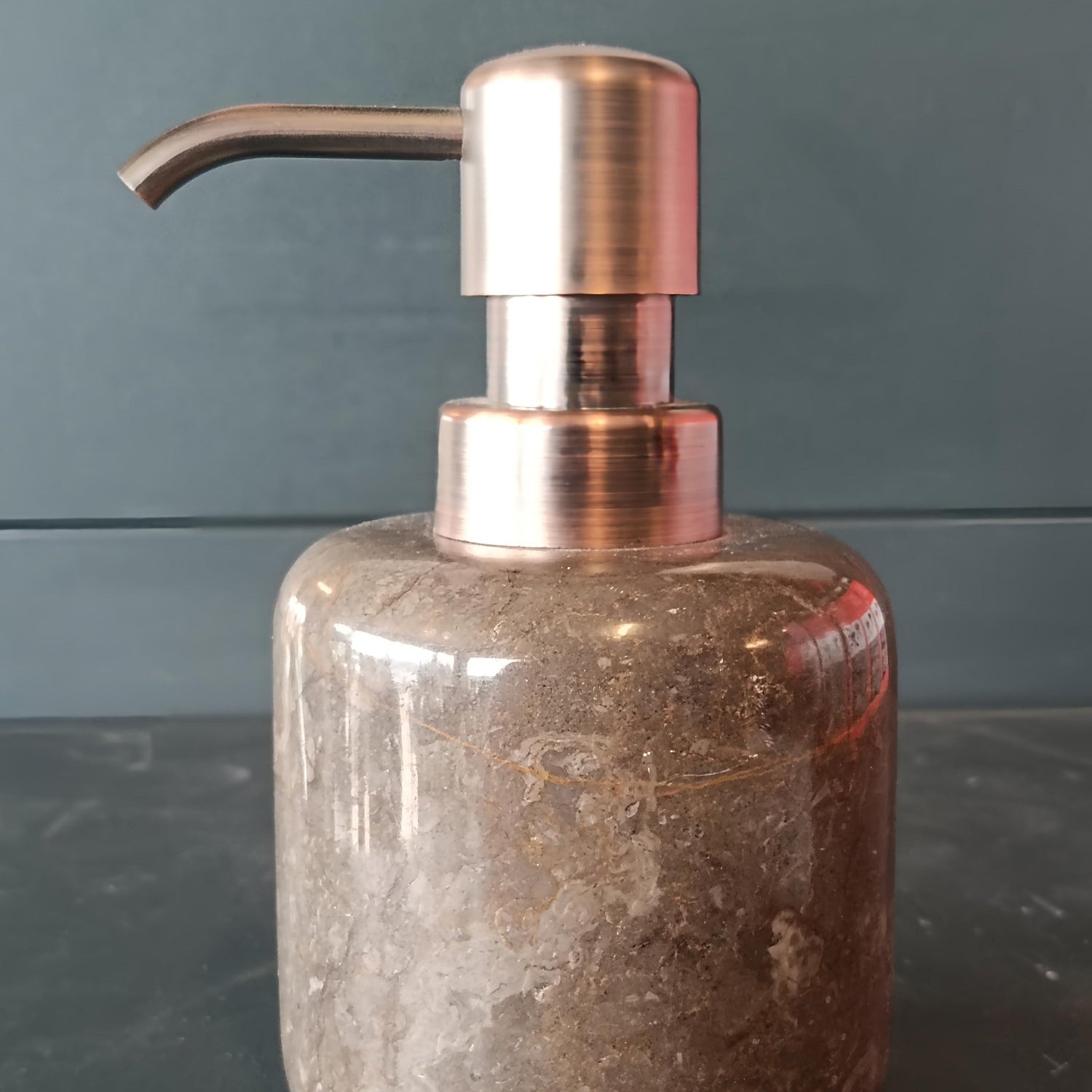Soap dispenser with bronze pump and textured brown body on a dark surface.