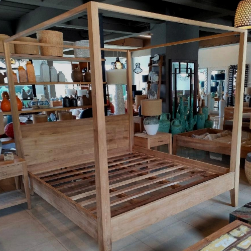 Wooden canopy bed in a store setting with various items on shelves.