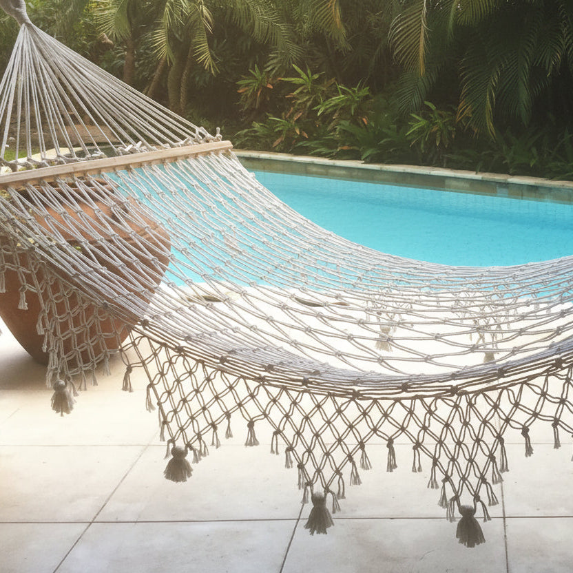 Textured woven hammock with tassels by a poolside