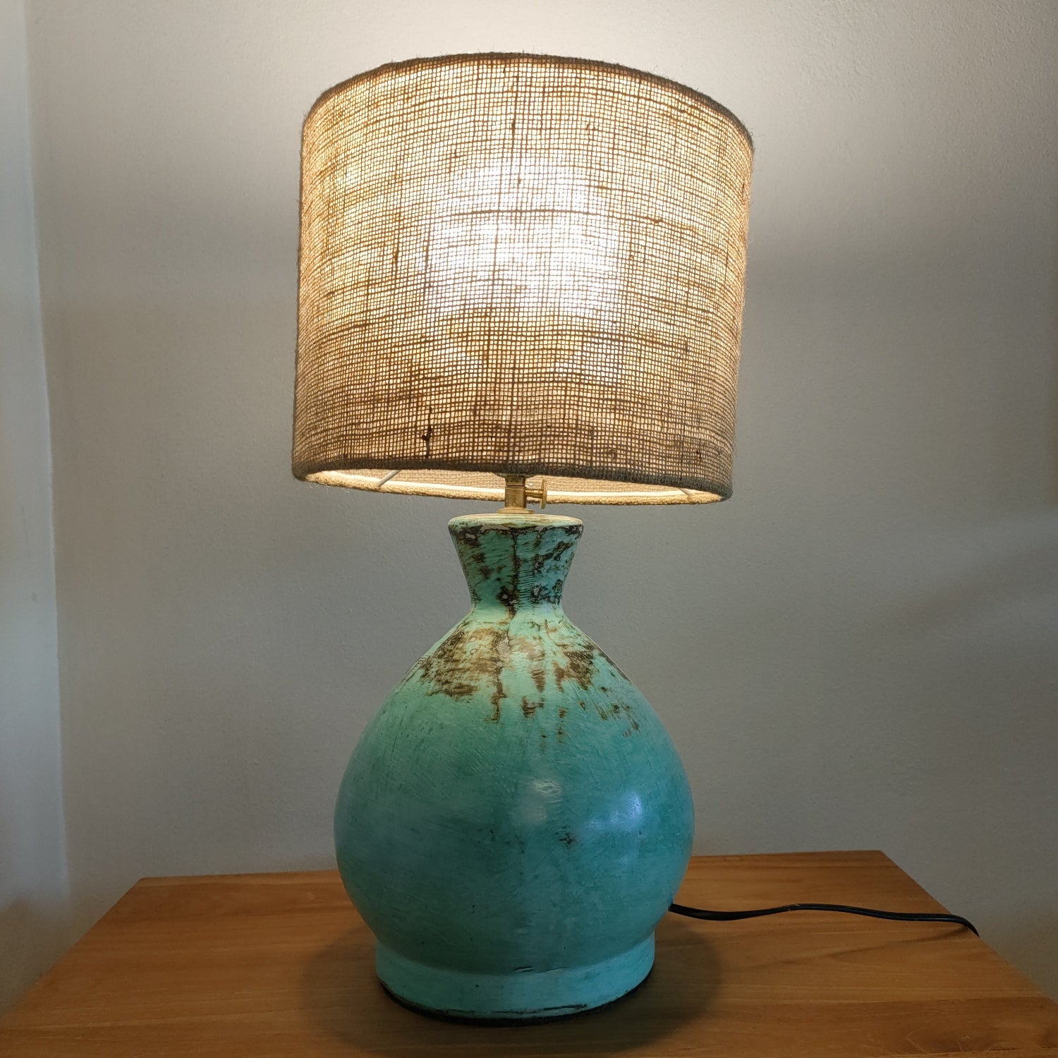 Turquoise table lamp with a wicker shade on a wooden surface.