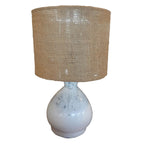 A bedside lamp with a hand-painted terracotta base in white color and a shade made of hemp, with a natural beige tone.