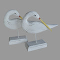 A pair of decorative wooden egrets perched on white bases, with a distressed white finish.