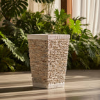 Decorative stone-patterned planter on a wooden surface with green plants in the background