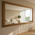 Large wooden-framed mirror on a wall in a living room with a couch and window.